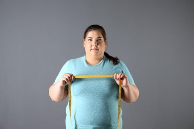 Overweight woman with measuring tape on gray background