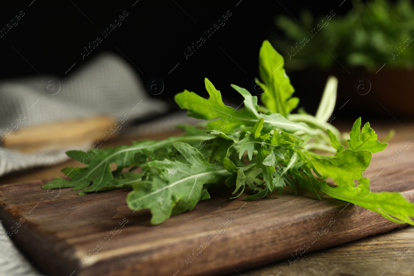 Photo of Fresh arugula and cutting board on wooden table, closeup