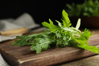 Fresh arugula and cutting board on wooden table, closeup