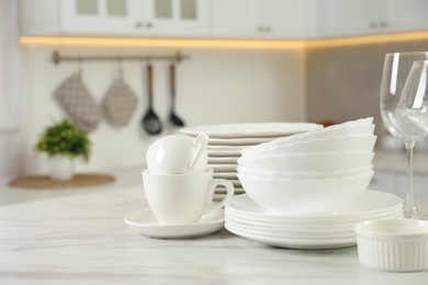 Photo of Clean plates, bowls, cups and glasses on white marble table in kitchen