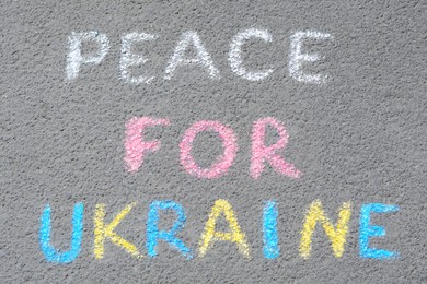 Photo of Words Peace For Ukraine written with colorful chalks on asphalt outdoors, top view