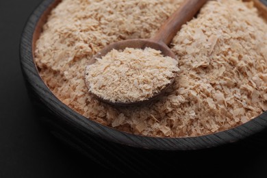 Photo of Bowl and spoon of brewer`s yeast flakes on black background, closeup
