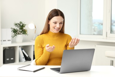 Woman having video chat via laptop at table in office