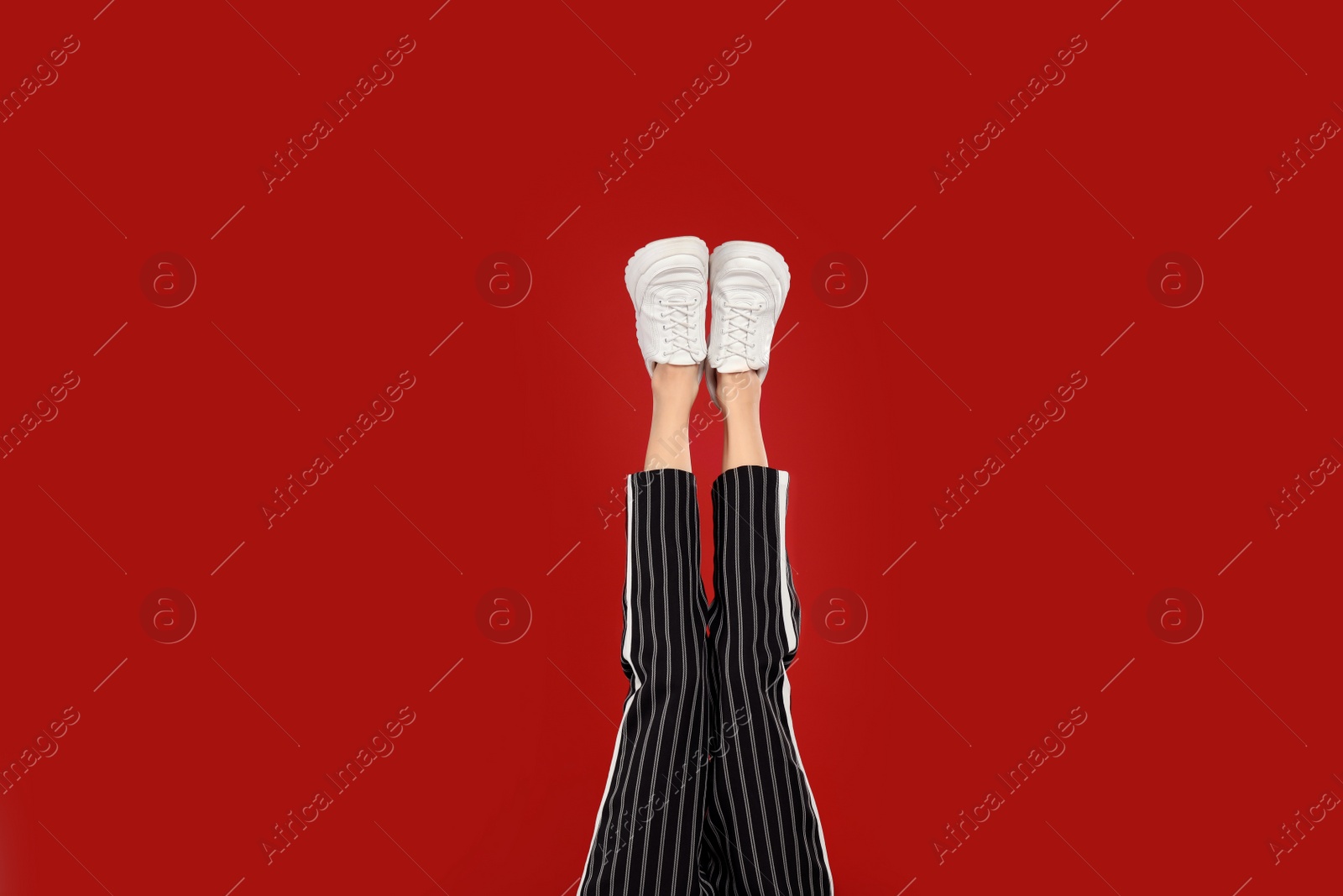 Photo of Woman in stylish sport shoes on red background