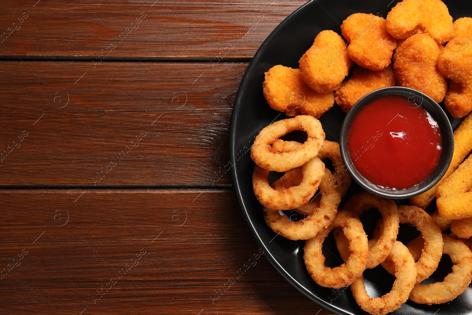 Photo of Plate with tasty ketchup and different snacks on wooden table, top view. Space for text