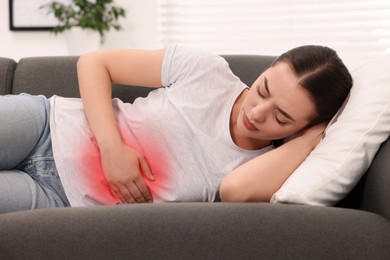 Image of Woman suffering from abdominal pain on sofa at home