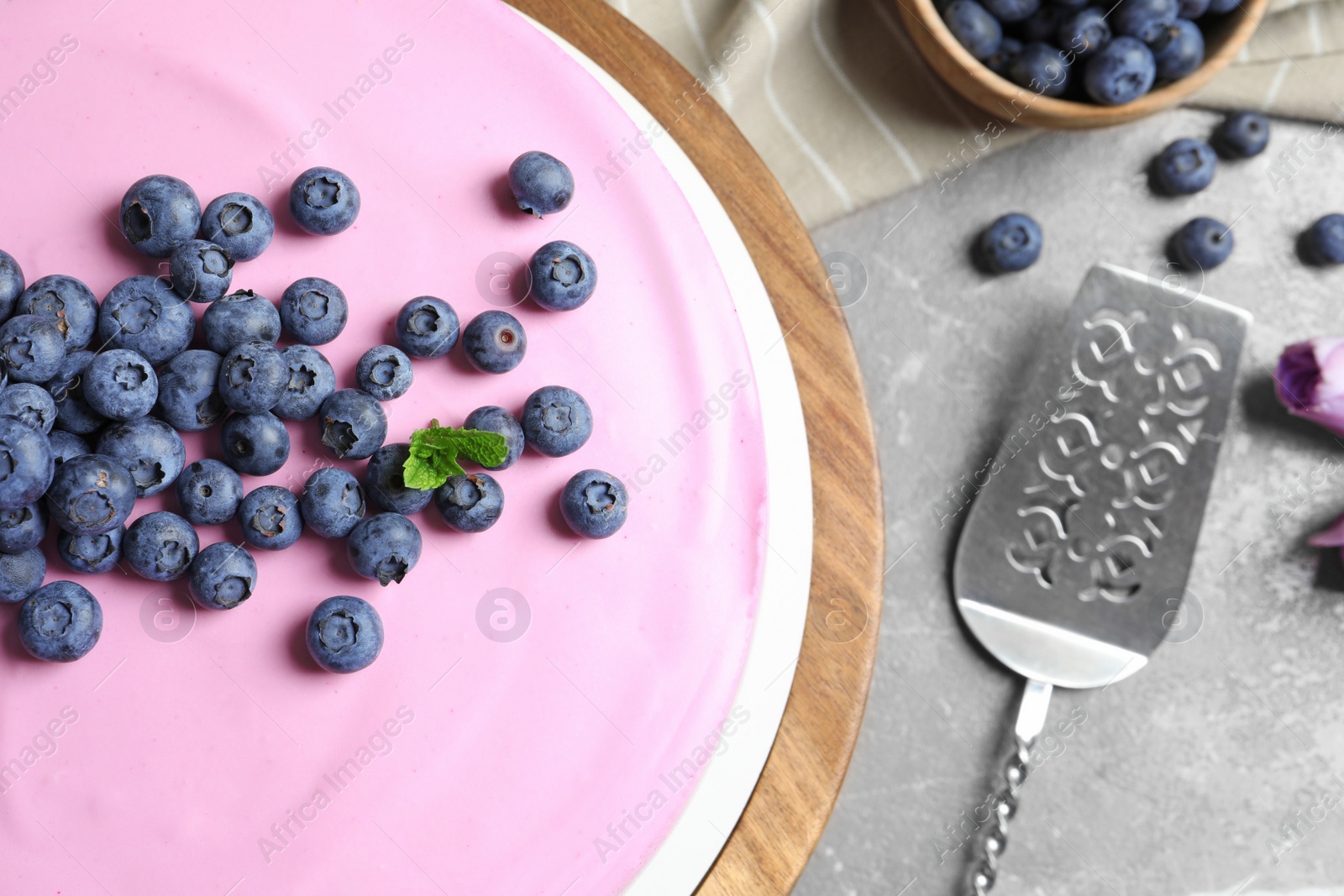 Photo of Wooden stand with tasty blueberry cake on grey table, flat lay