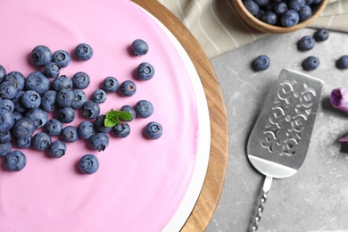 Photo of Wooden stand with tasty blueberry cake on grey table, flat lay