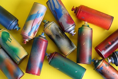 Many spray paint cans on yellow background, flat lay