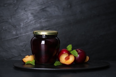 Photo of Glass jar of pickled plums and fresh fruits on black table