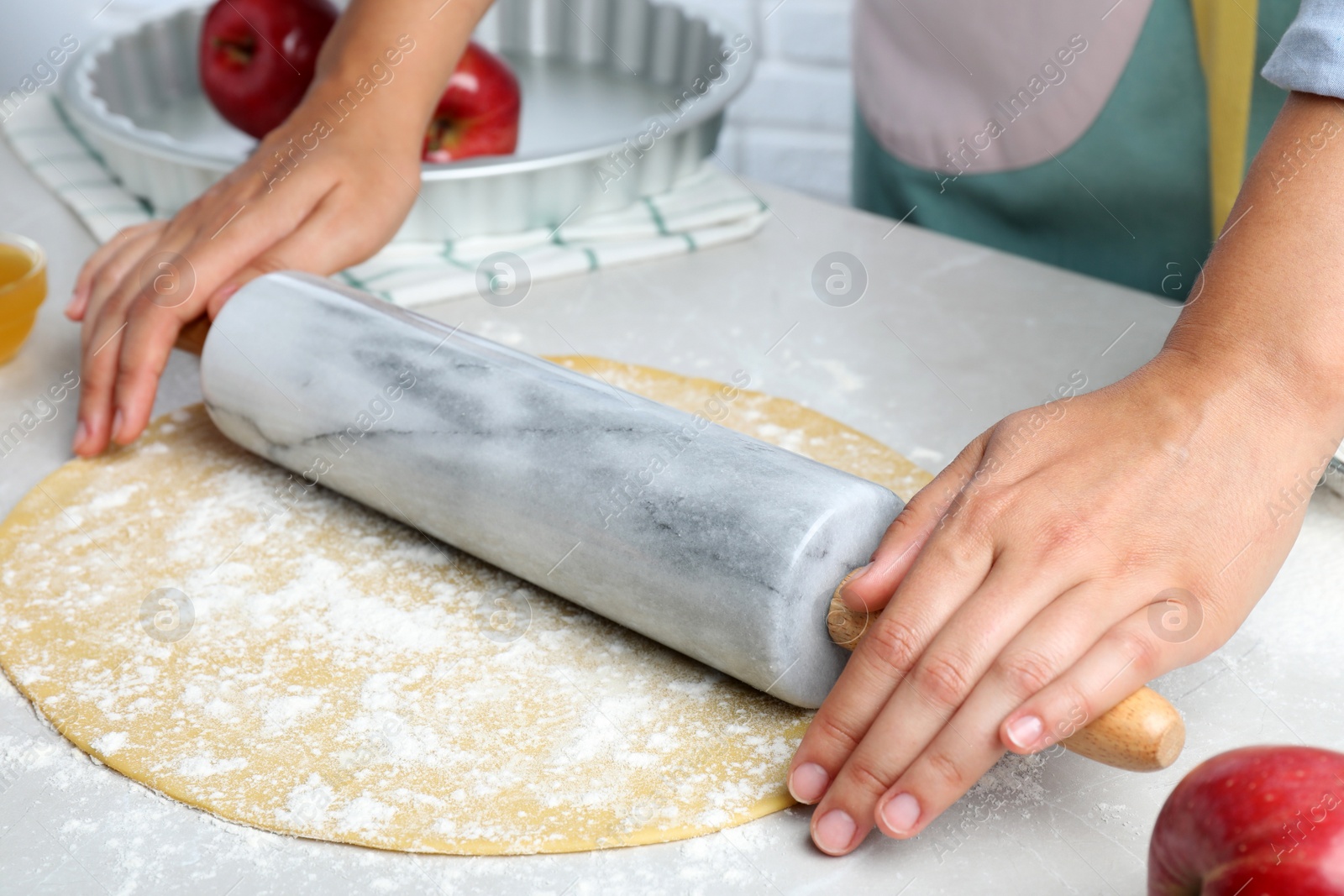 Photo of Woman rolling dough for apple pie at light grey table, closeup