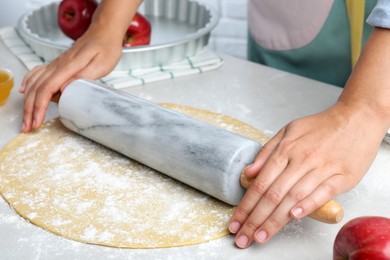 Woman rolling dough for apple pie at light grey table, closeup