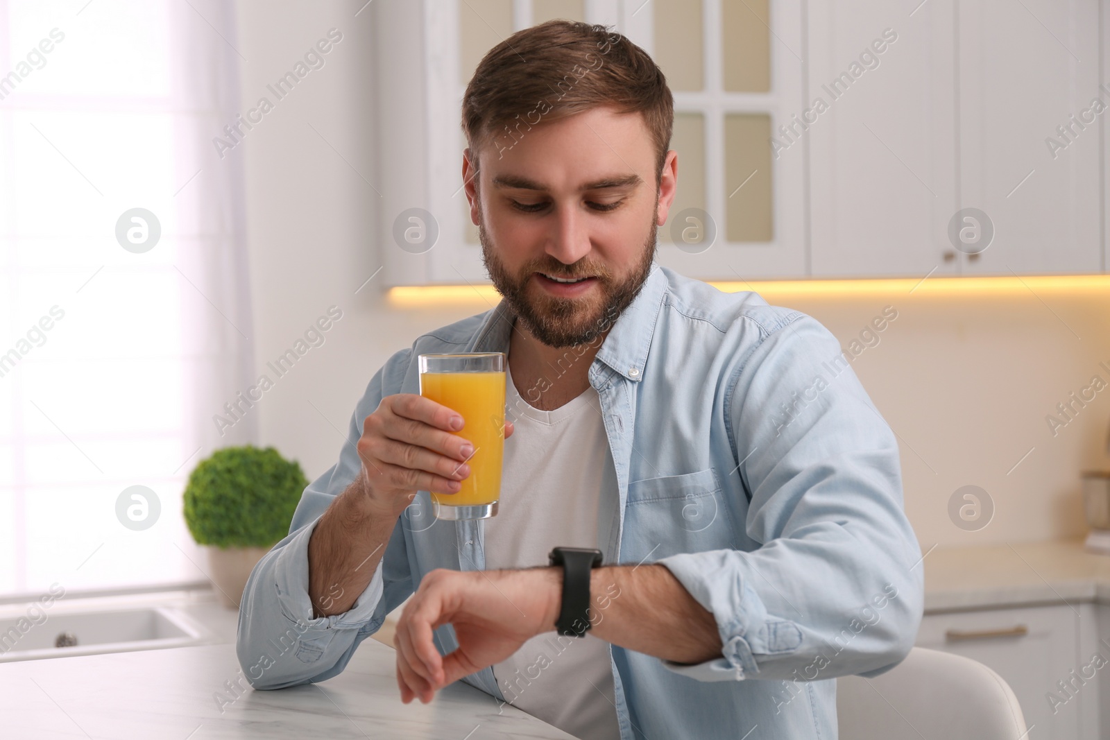 Photo of Young man with smart watch and glass of juice in kitchen