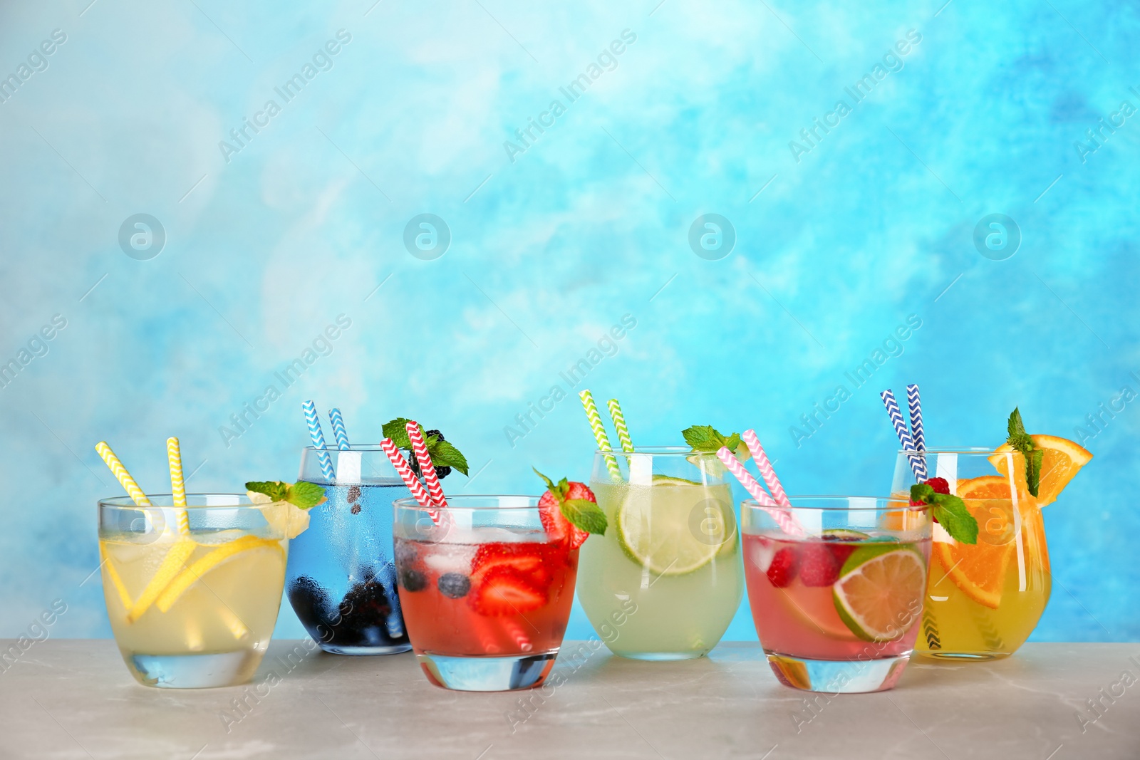 Photo of Glasses with lemonades on table against color background