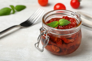 Photo of Jar with sun dried tomatoes on light table. Space for text
