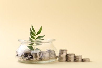 Photo of Financial savings. Coins, twig and glass jar on beige background