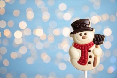 Funny chocolate snowman candy against blurred festive lights, closeup. Space for text