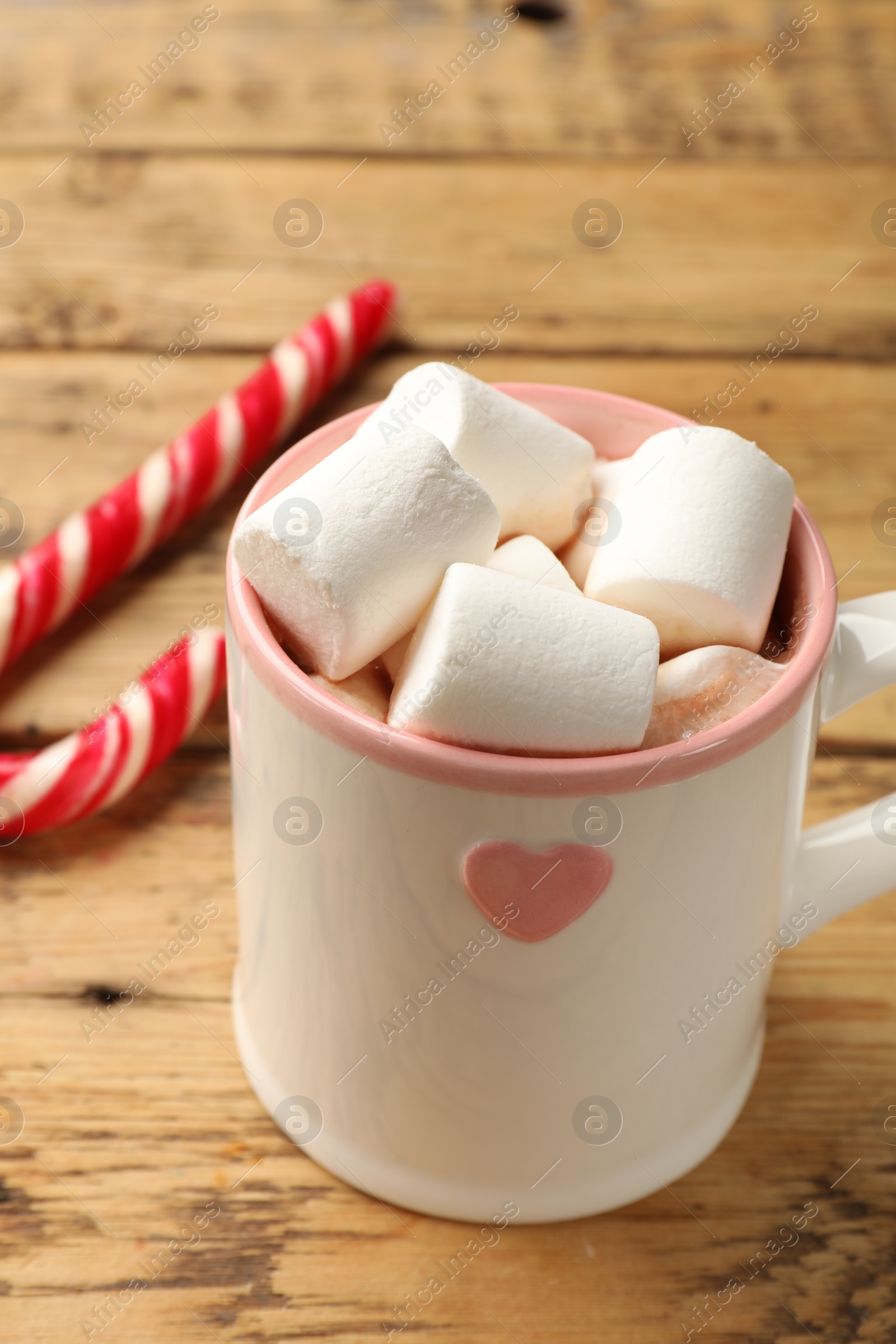 Photo of Tasty hot chocolate with marshmallows and candy cane on wooden table, closeup