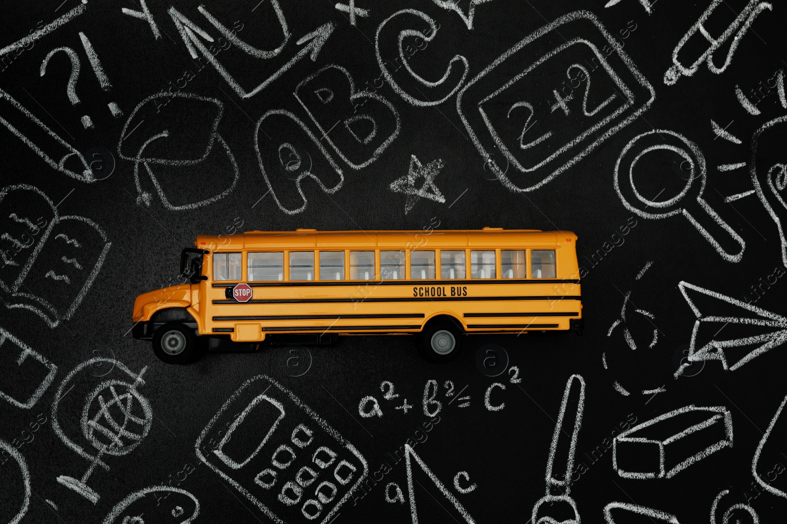 Photo of Yellow school bus and doodles on chalkboard, top view. Transport for students
