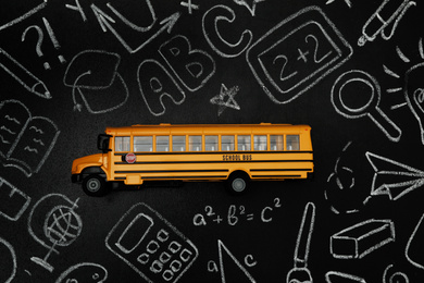 Photo of Yellow school bus and doodles on chalkboard, top view. Transport for students