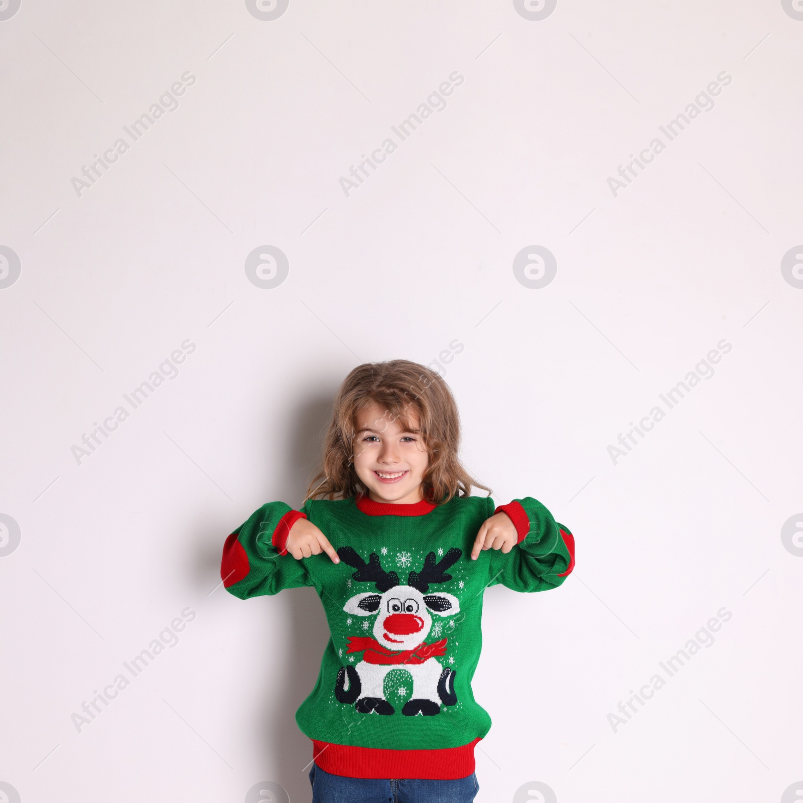 Photo of Cute little girl pointing at her green Christmas sweater against white background