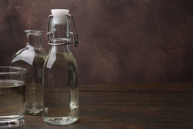 Photo of Vinegar in bottles and glass on wooden table, space for text