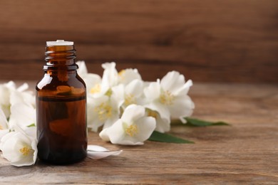 Photo of Jasmine essential oil and fresh flowers on wooden table, space for text