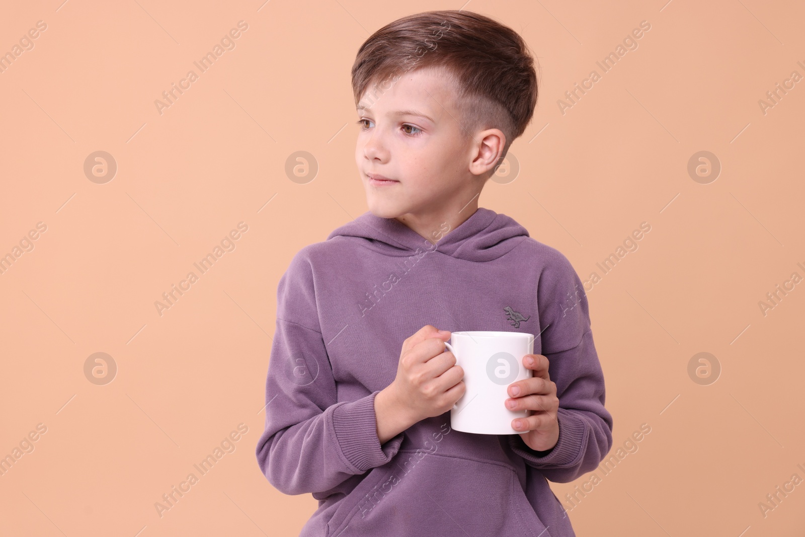 Photo of Cute boy with white ceramic mug on beige background