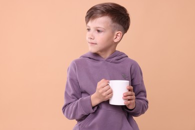 Photo of Cute boy with white ceramic mug on beige background