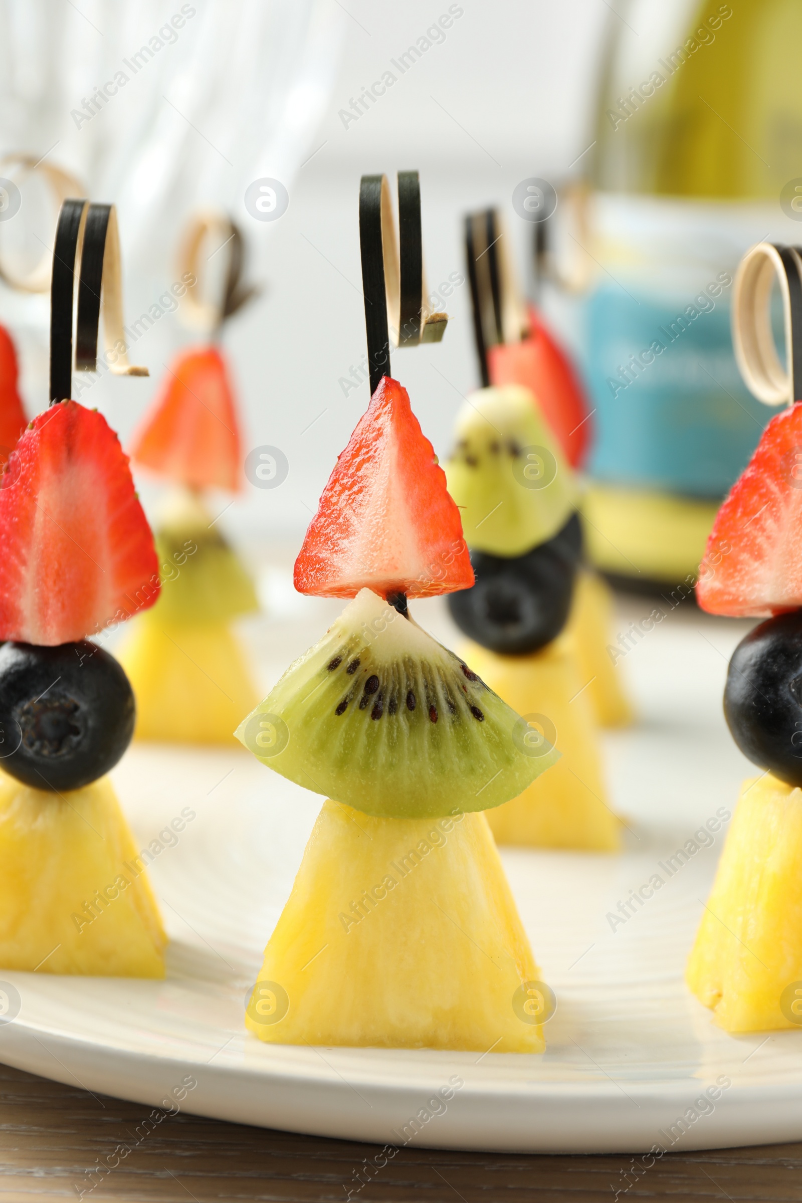 Photo of Tasty canapes with pineapple, kiwi and berries on light wooden table, closeup