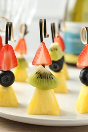 Photo of Tasty canapes with pineapple, kiwi and berries on light wooden table, closeup