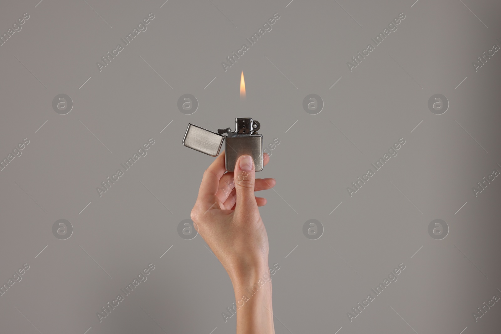 Photo of Woman holding lighter with burning flame on grey background, closeup