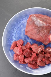 Photo of Plate with pieces of raw beef meat on grey textured table, top view