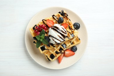Photo of Delicious Belgian waffles with ice cream, berries and chocolate sauce served on white wooden table, top view