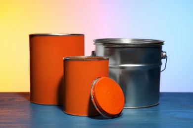 Cans and bucket of orange paint on wooden table against color background