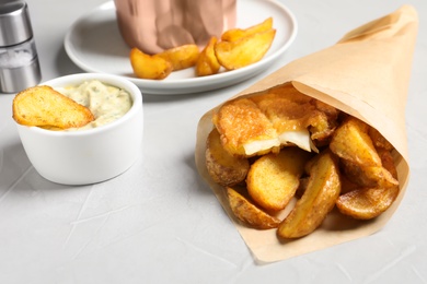 Photo of British traditional fish and potato chips in paper cone on table