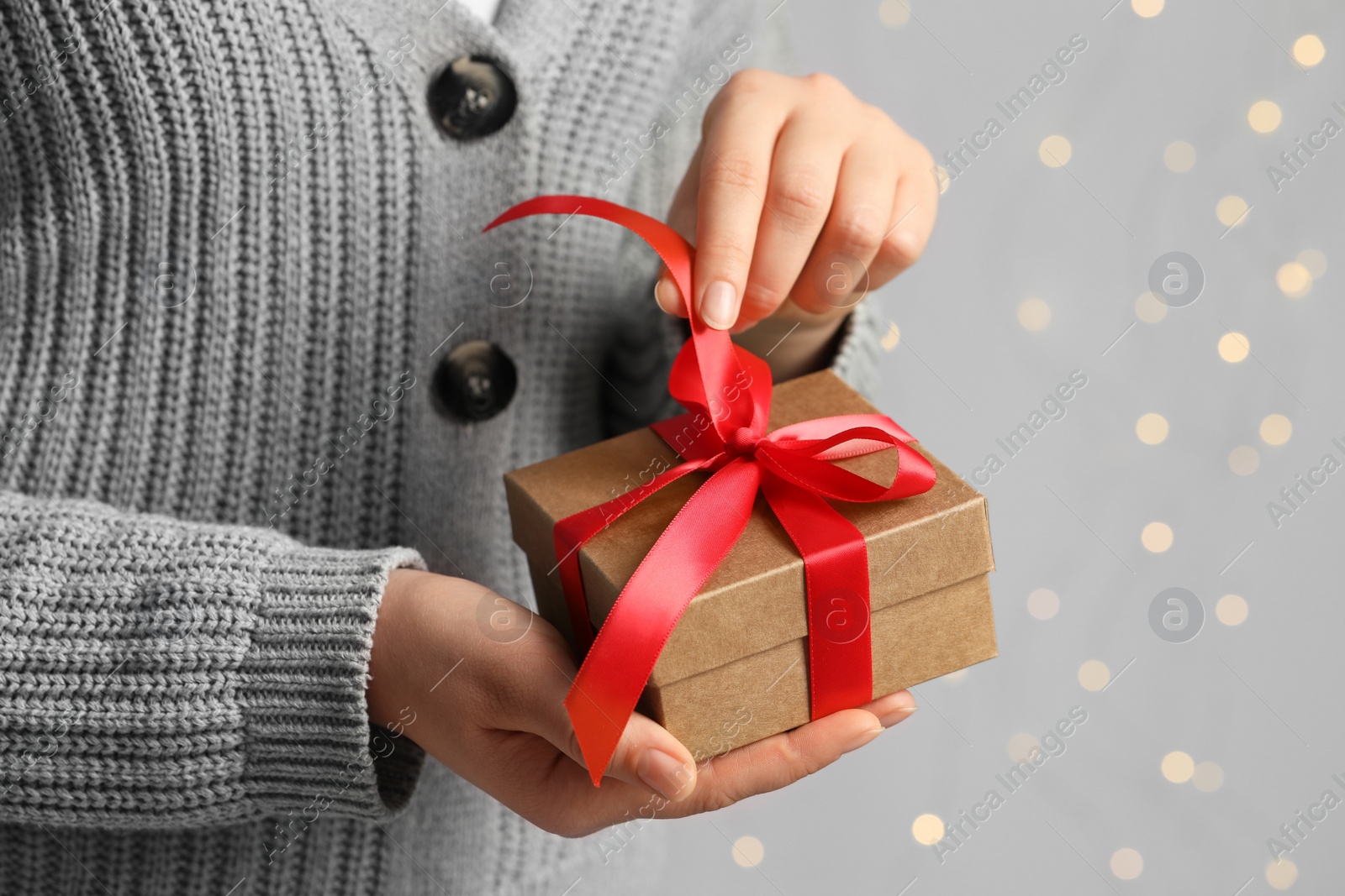 Photo of Woman holding gift box with red bow against blurred festive lights, closeup and space for text. Bokeh effect