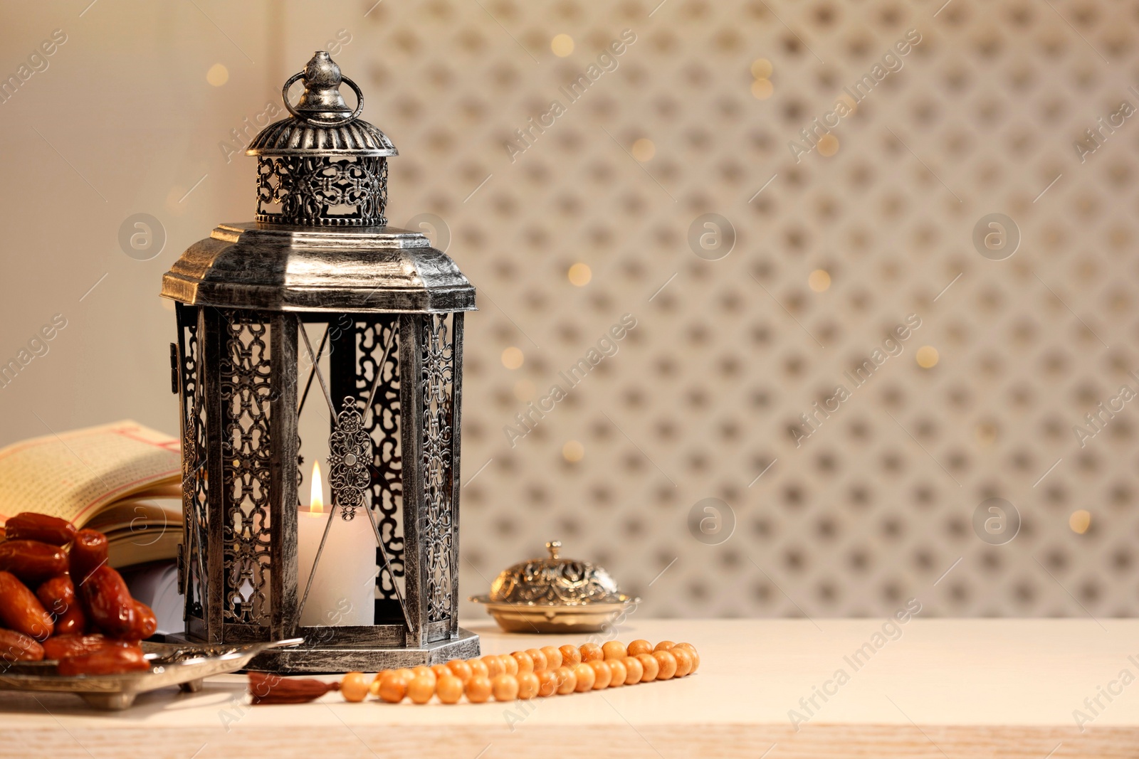 Photo of Arabic lantern, Quran, misbaha and dates on white table. Space for text