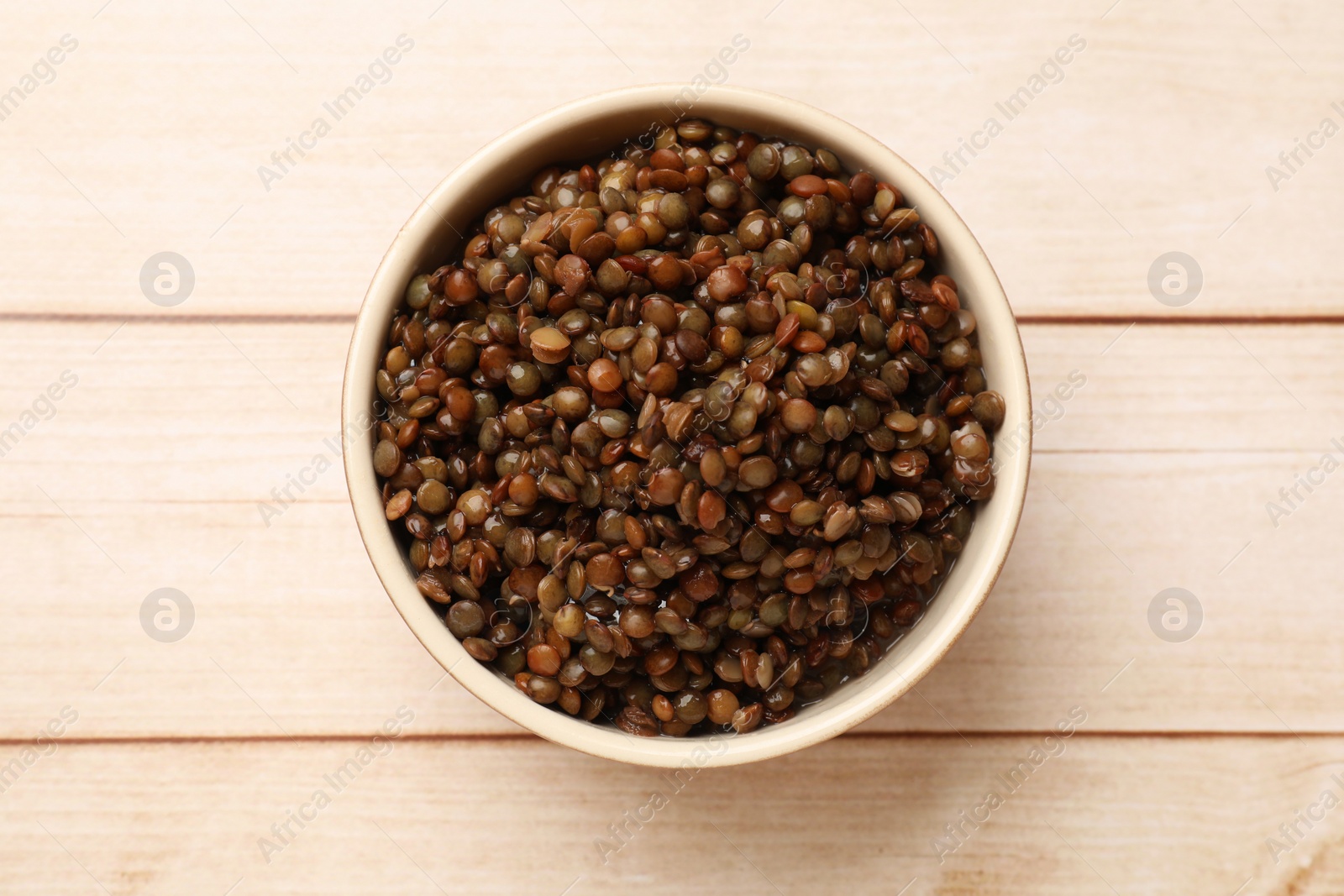 Photo of Delicious lentils in bowl on wooden table, top view