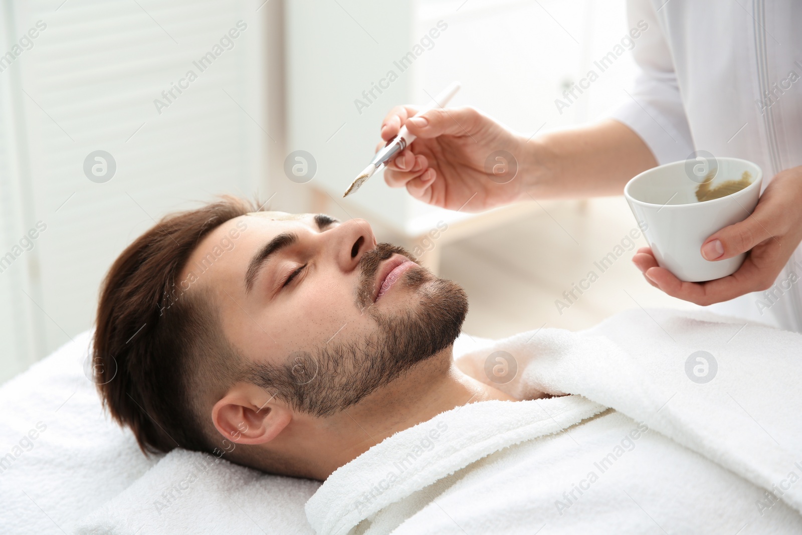 Photo of Cosmetologist applying mask on client's face in spa salon