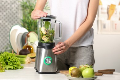 Photo of Woman preparing tasty green smoothie at white wooden table in kitchen, closeup