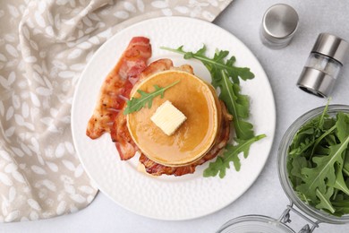 Delicious pancakes with bacon, butter and arugula on light table, flat lay