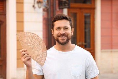 Happy man holding hand fan on city street