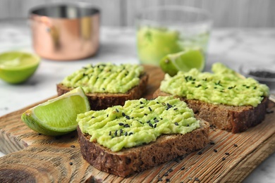 Photo of Crisp rye toasts with avocado on wooden board, closeup