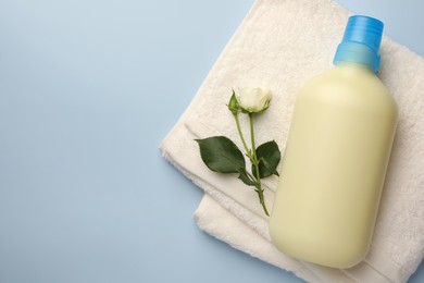 Photo of Bottle of fabric softener, terry towel and beautiful rose on light background, top view. Space for text
