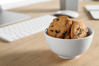 Photo of Chocolate chip cookies on wooden table at workplace, closeup. Space for text