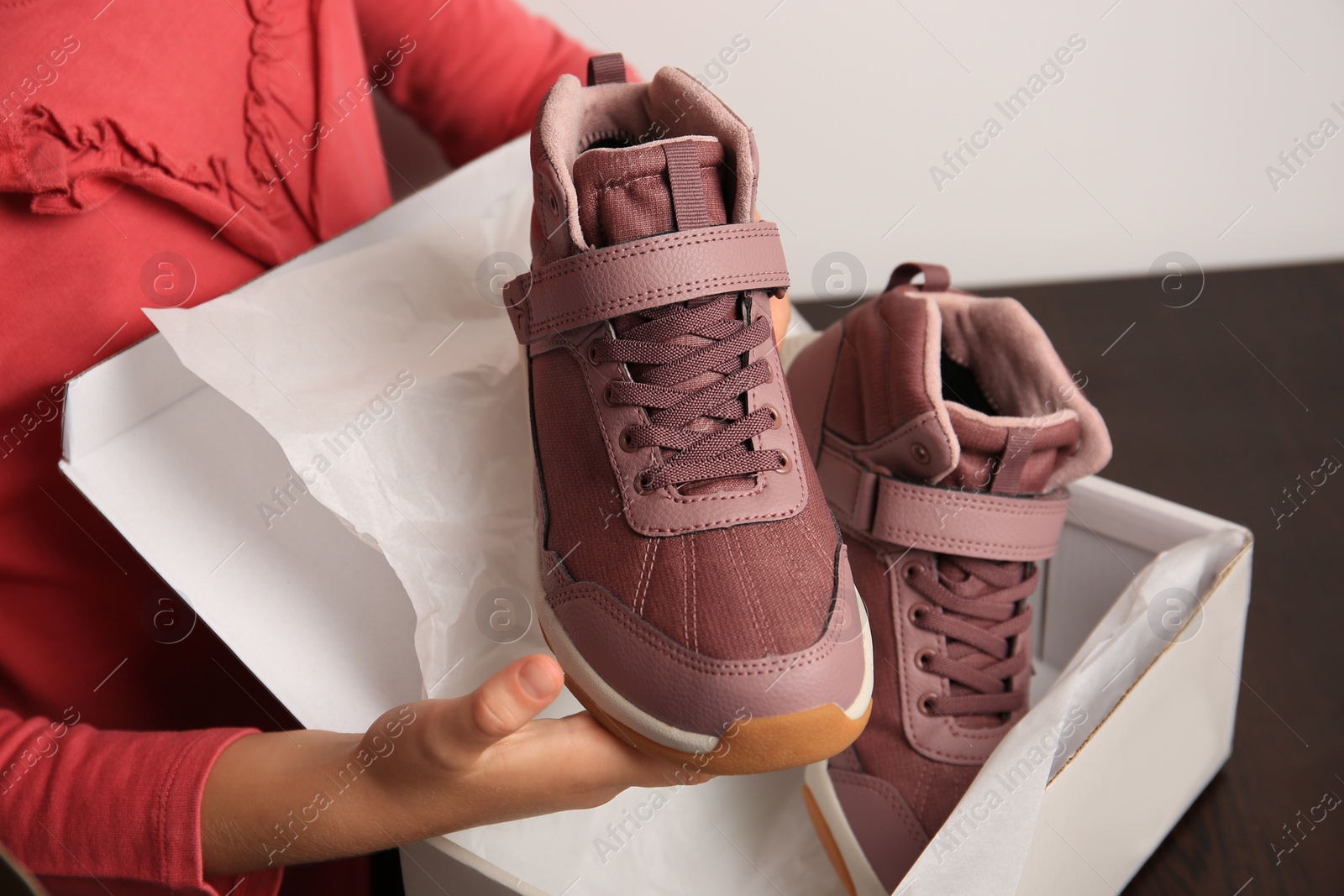 Photo of Girl taking out new sneakers from box at wooden table against light grey background, closeup