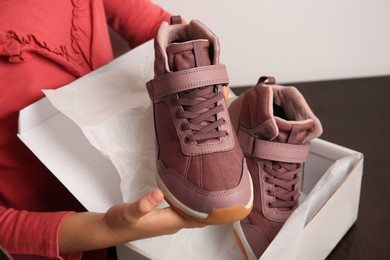 Photo of Girl taking out new sneakers from box at wooden table against light grey background, closeup