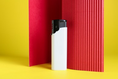 Photo of Stylish small pocket lighter and red corrugated fiberboard on yellow background