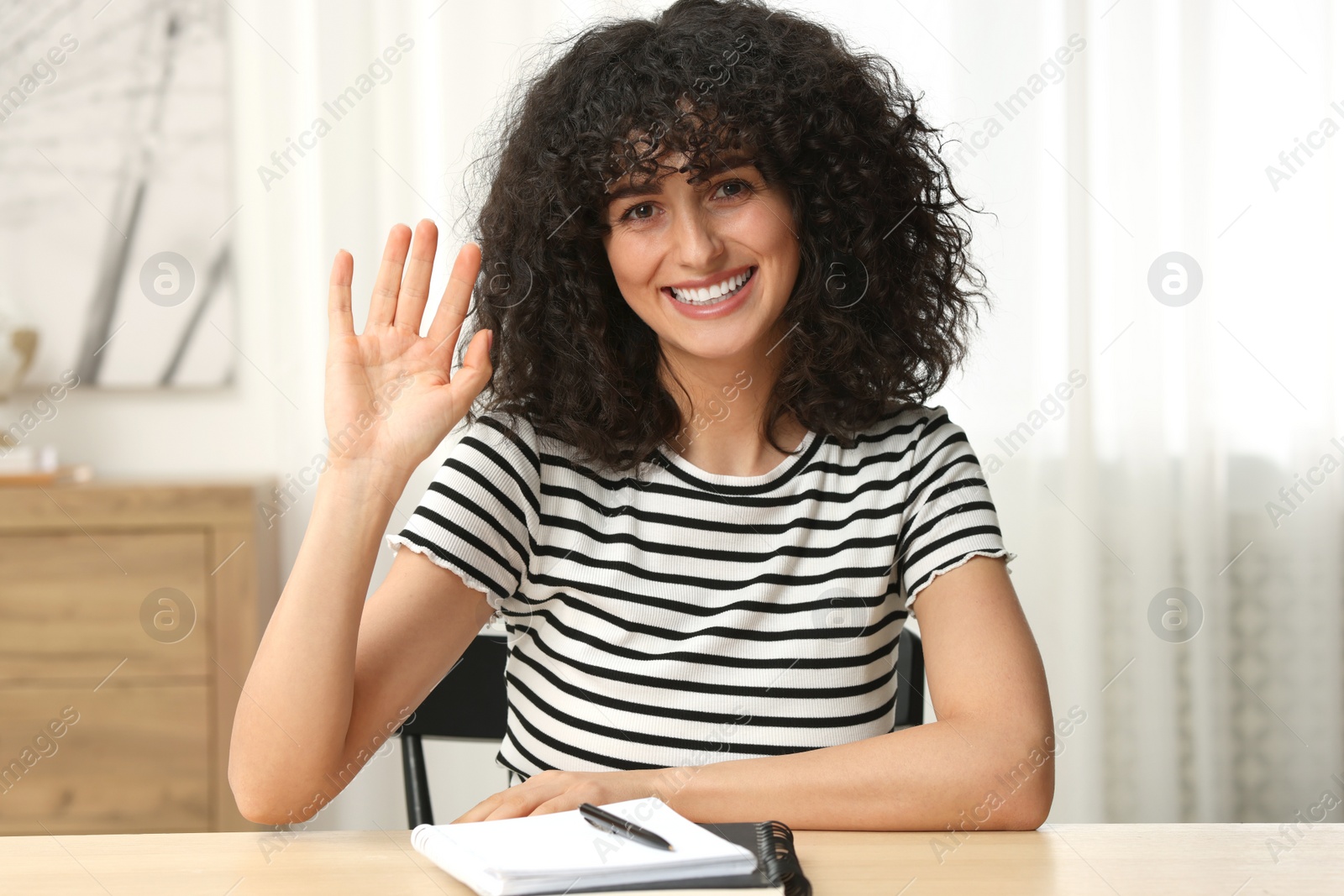 Photo of Happy woman waving hello at wooden table in room